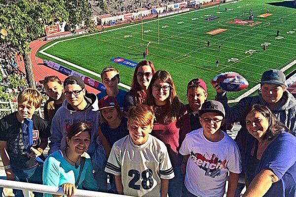 Intervenantes et groupe d'une dizaine de jeune devant le terrain du Stade Mémorial Percival-Molson pour une partie des Alouettes de Montréal