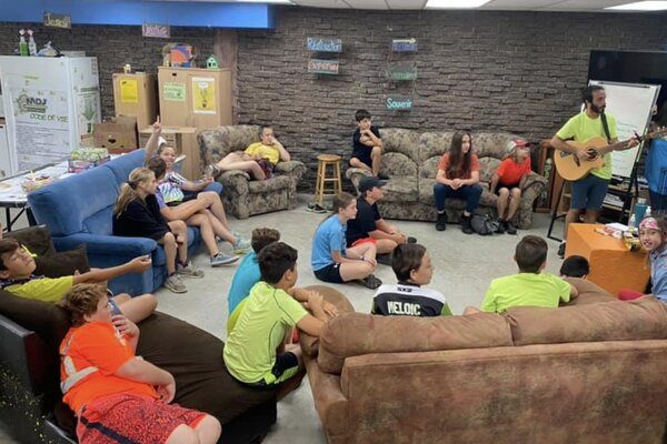 Intervenant qui joue de la guitare pour 16 jeunes dans le milieu de vie à la maison des jeunes