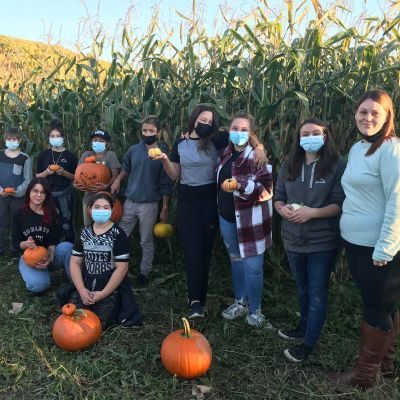 Groupe de 9 jeunes et une intervenante dans un champ de blé d'inde avec des citrouilles