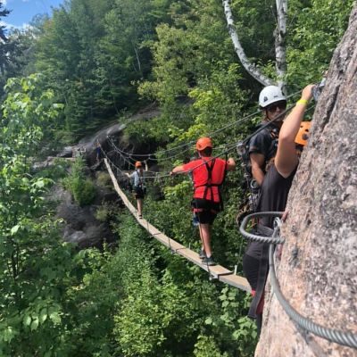 3 jeunes participant à un parcours de via ferrata sur une paroi rocheuse au dessus des arbres