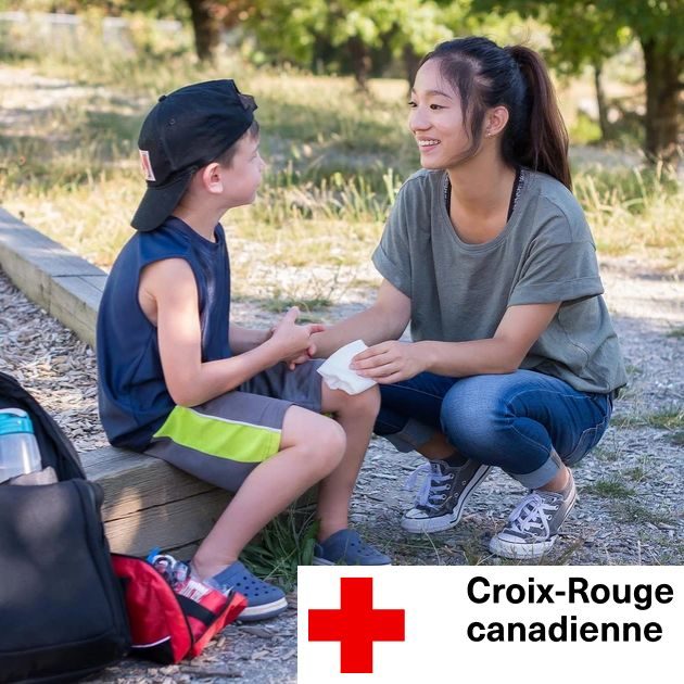 Adolescente qui applique une compresse sur le genou d'un jeune garçon avec le logo de la Croix-Rouge canadienne